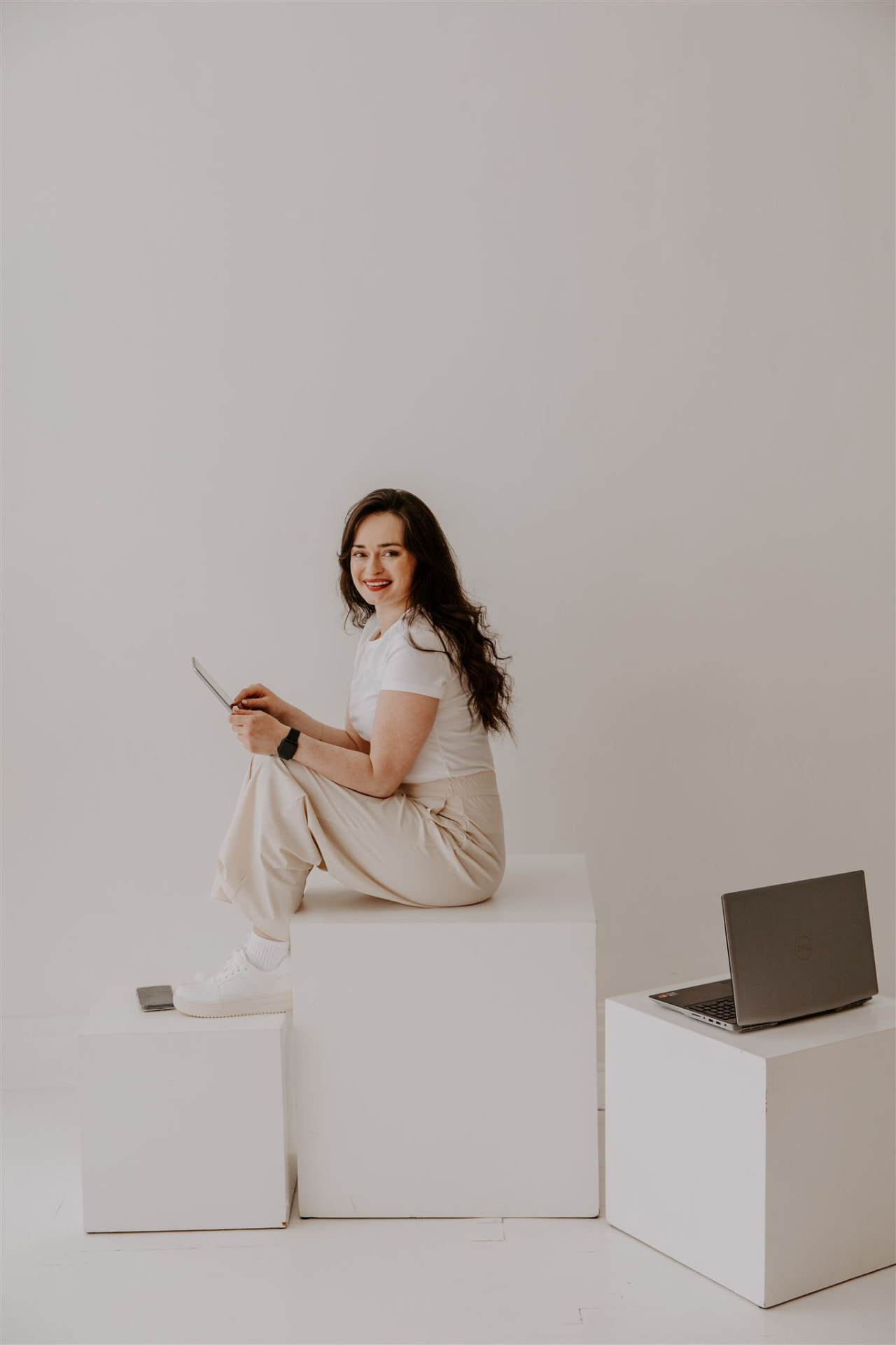 Kat seated on a white studio block with a tablet